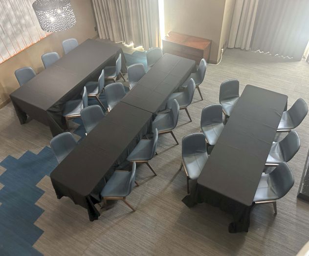 The image shows a conference room with tables arranged in a U-shape, covered with black tablecloths, and surrounded by gray chairs.