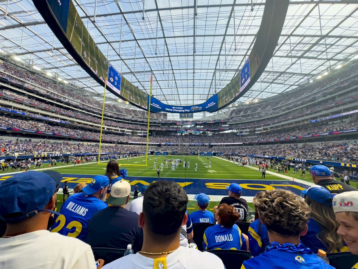 A crowded football stadium with fans wearing team jerseys, watching a game, with a large digital screen above.
