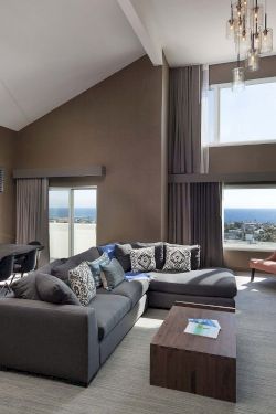 A modern, open-concept living area with a gray sectional, floor-to-ceiling windows, a fireplace, and a dining space&mdash;cozy and stylish, with a view.